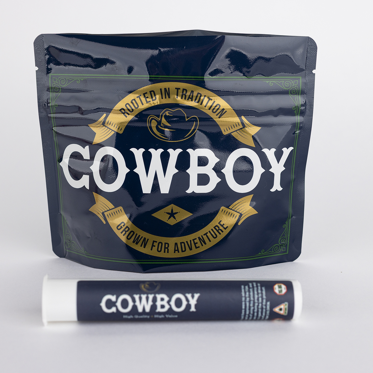 Premium cannabis packaging by Cowboy Kush featuring a resealable marijuana flower pouch and a pre-roll joint tube resting on a rustic wooden tree stump outdoors.
