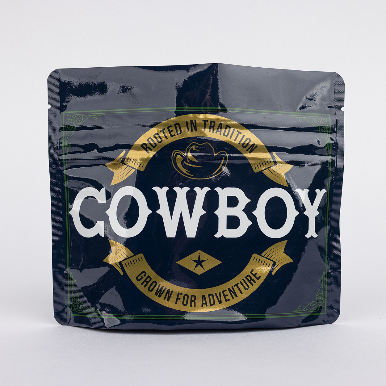 Premium Cowboy Kush cannabis flower packaging featuring a resealable black pouch with the gold and white "Rooted in Tradition, Grown for Adventure" branding, isolated on a white background.
