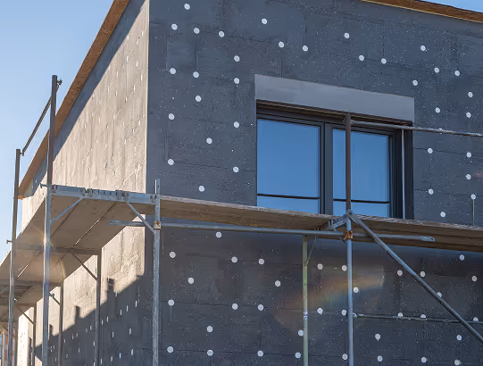 Hauswand mit Wärmedämmung und Gerüst, sichtbare Dämmplatten und Fenster.