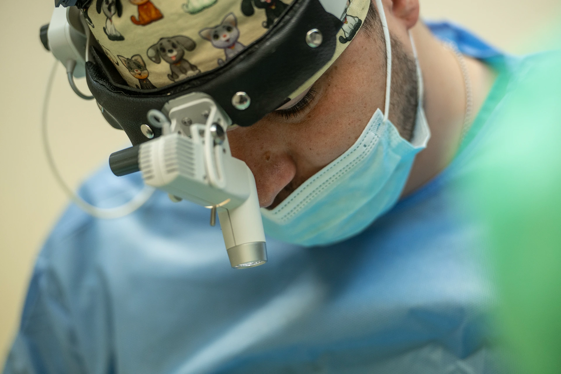 Close-up of a surgeon wearing a lighted headlamp and a blue surgical mask during an operation.