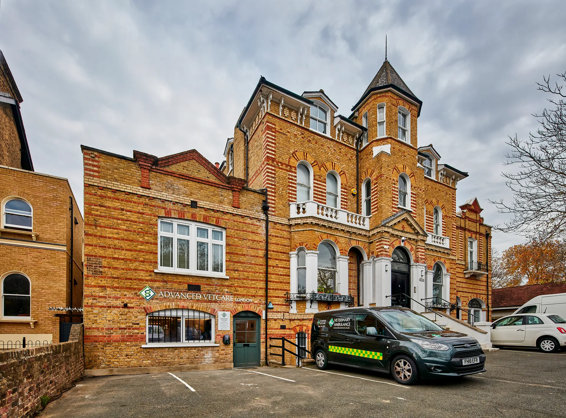 Brick building housing Advanced Vetcare London with a veterinary ambulance van parked outside on a cloudy day.