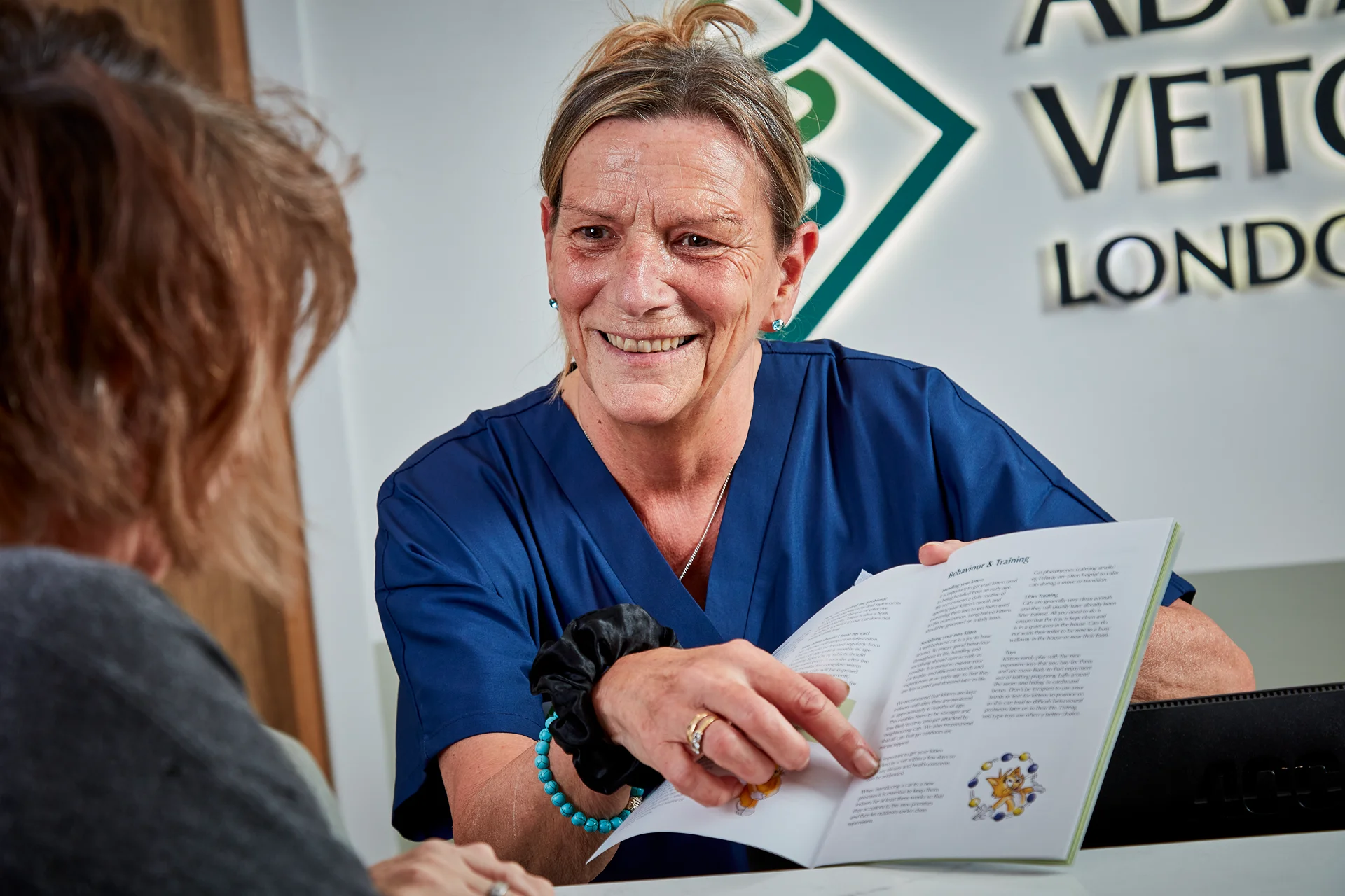 Veterinary professional in blue scrubs showing a booklet with pet care tips to a client.
