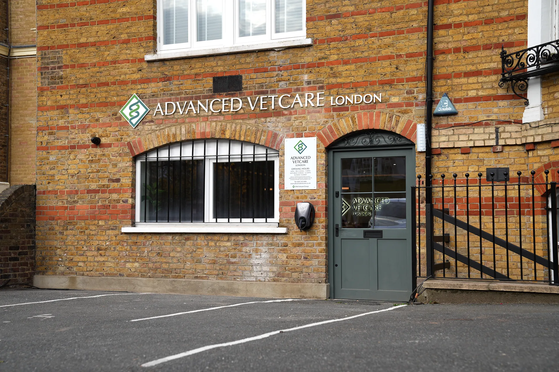 Brick building facade with a green door and window bars, displaying the sign 'Advanced Vetcare London' above the door and window.