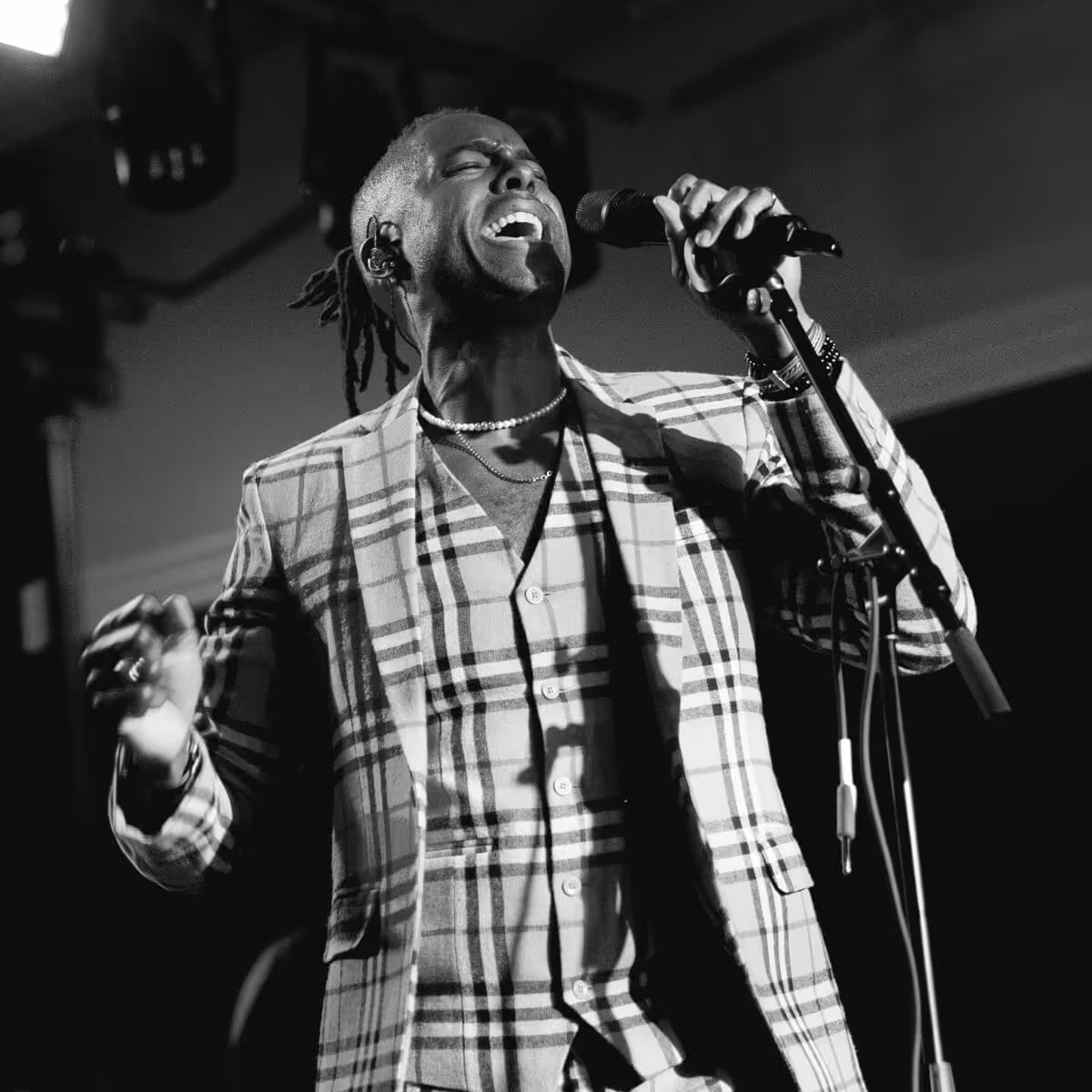Black-and-white photo of a male singer passionately performing with eyes closed, wearing a plaid suit and holding a microphone.