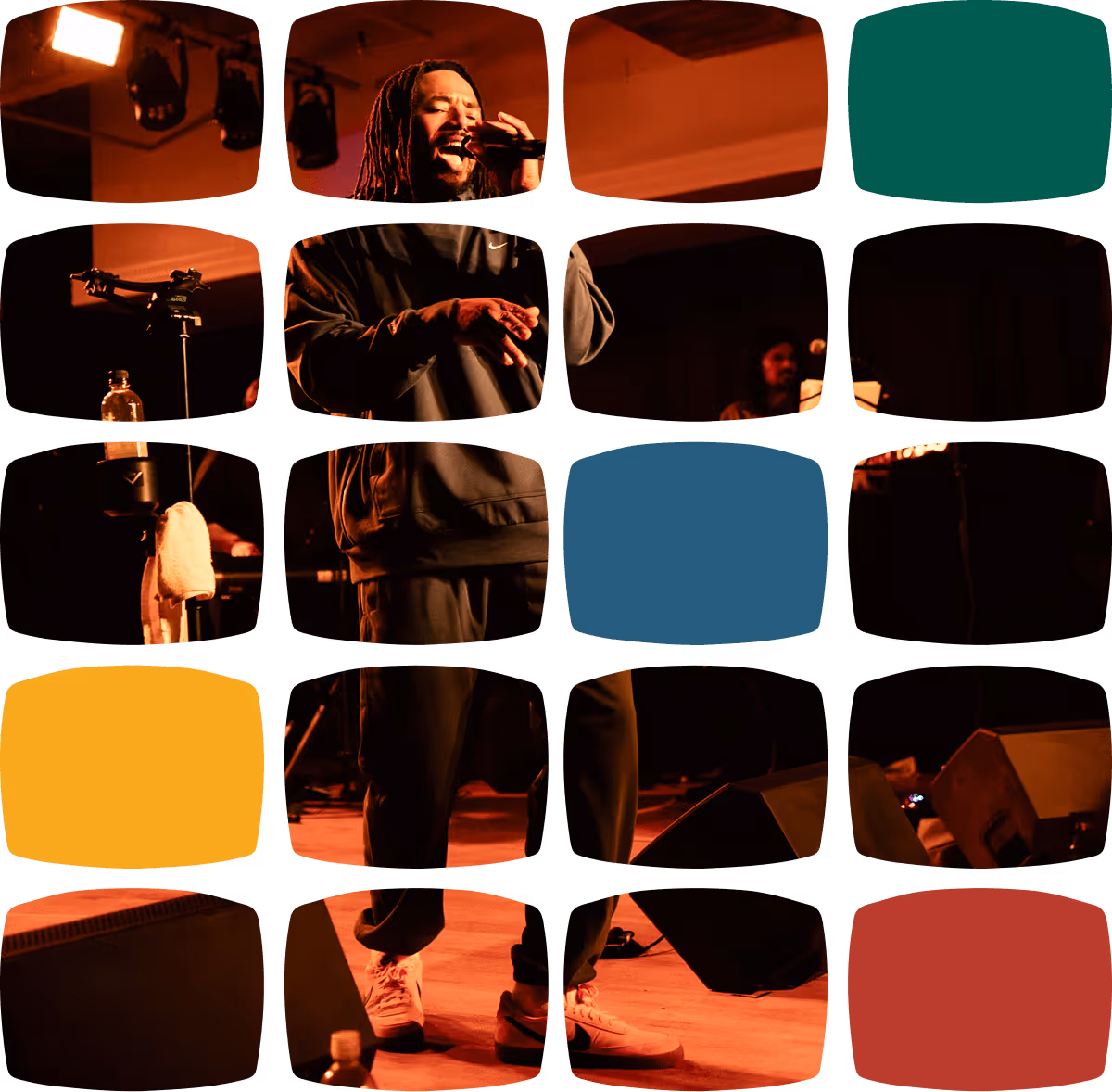 Singer in dark clothing performing on stage with microphone and band in background under warm lighting.