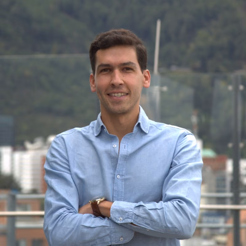 Ejecutivo sonriendo con los brazos cruzados, frente a un paisaje urbano montañoso.