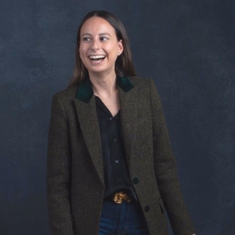 Ejecutiva sonriendo, vestida con chaqueta de lana y camisa negra, frente a fondo oscuro.