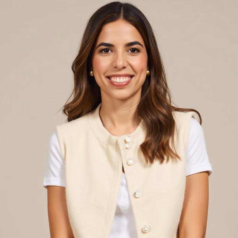 Mujer sonriente con un chaleco claro, frente a un fondo neutro, transmitiendo confianza y profesionalismo.