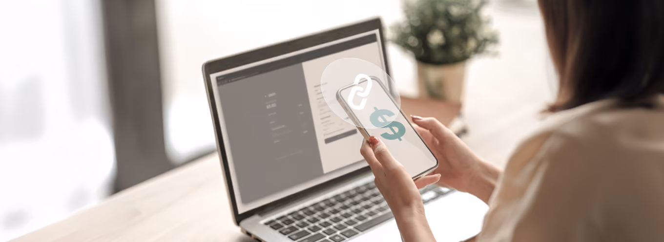 Mujer utilizando un smartphone con un ícono de enlace y dólar, frente a una laptop en un entorno moderno.