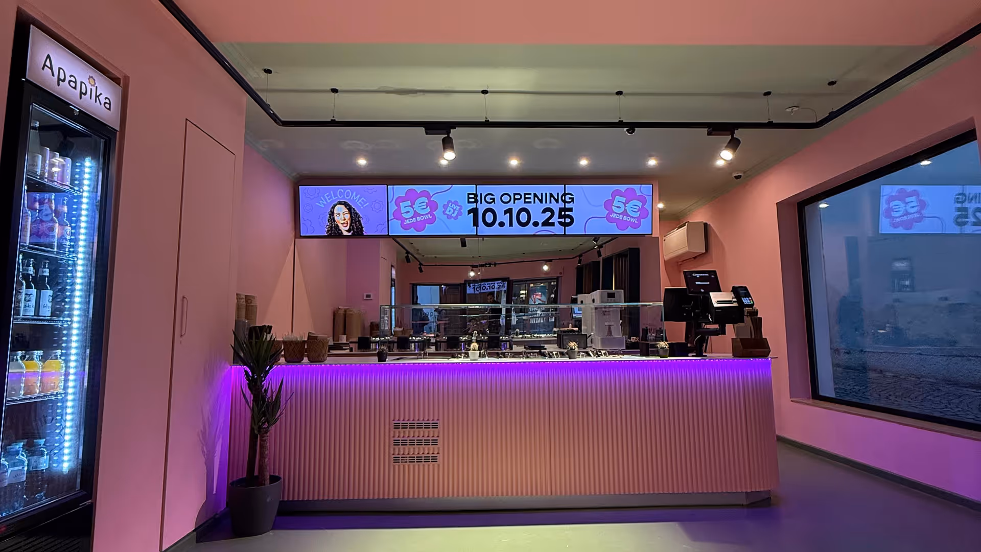 Rosafarbenes Café-Interieur mit moderner Theke, die von violetten Lichtern beleuchtet wird. 