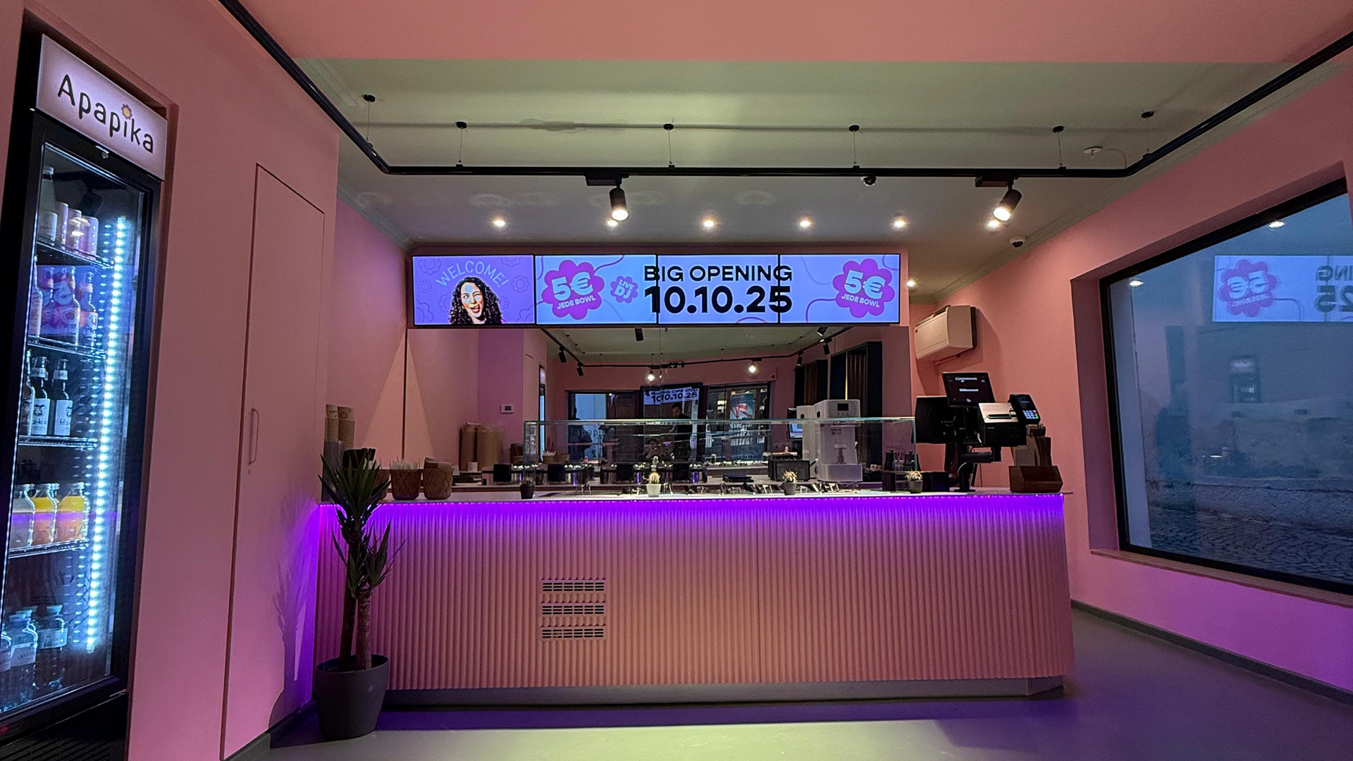 Rosafarbenes Café-Interieur mit moderner Theke, die von violetten Lichtern beleuchtet wird.