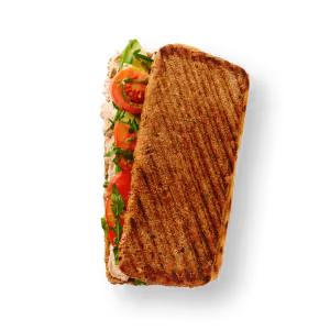 Ein gegrilltes Panini-Sandwich mit sichtbaren Schichten von Rucola, Tomatenscheiben und cremigem Aufstrich auf geröstetem Brot vor schwarzem Hintergrund.