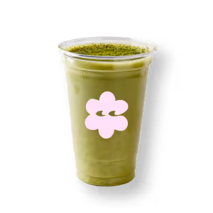 Ein durchsichtiger Plastikbecher gefüllt mit Eiskaffee-Matcha, bestreut mit grünem Pulver. Der Becher ziert ein rosafarbenes Blumenlogo. Vor einem einfarbig schwarzen Hintergrund.