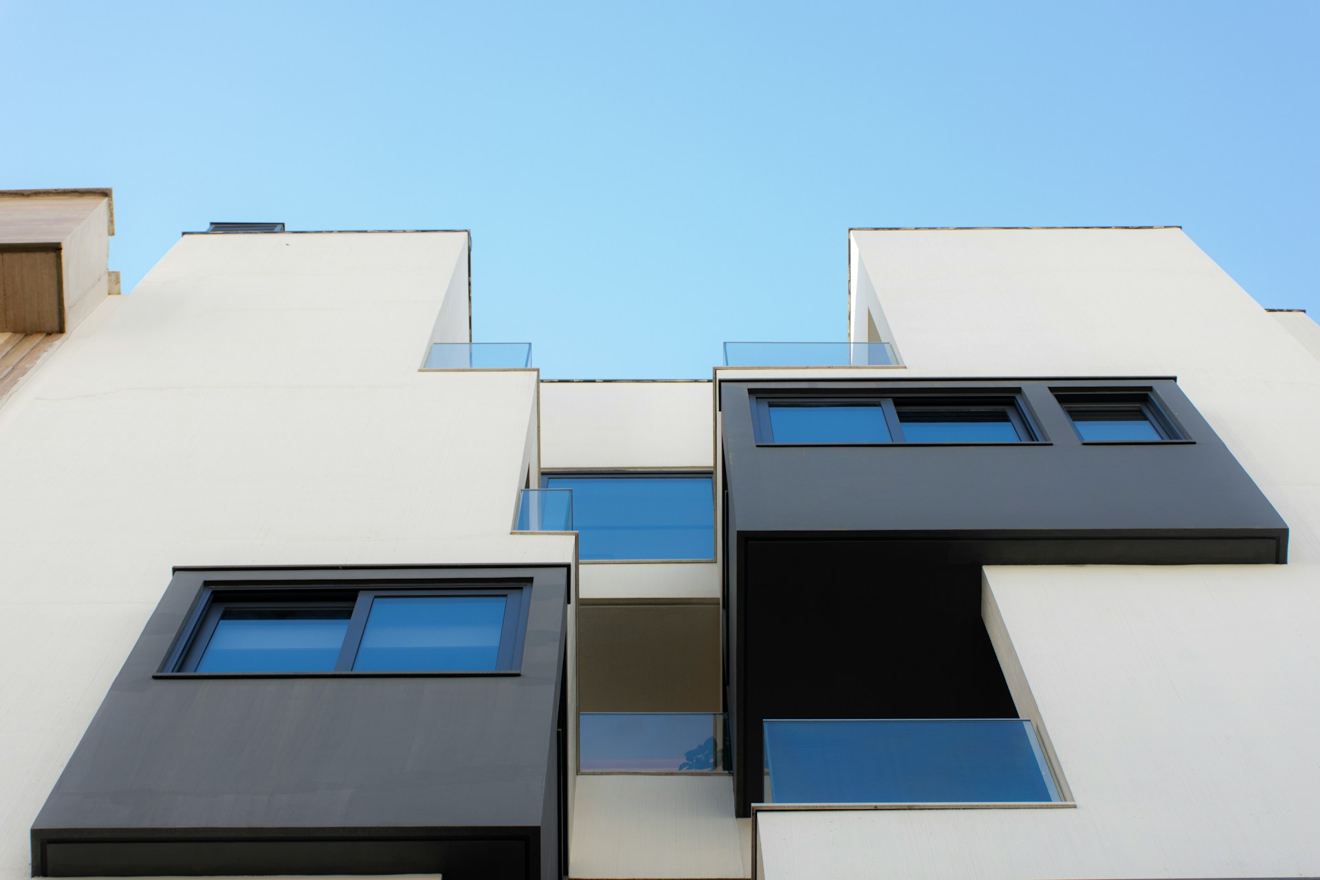 Modern new-build UK apartments with white render, black-framed windows, and glass balconies against a blue sky.