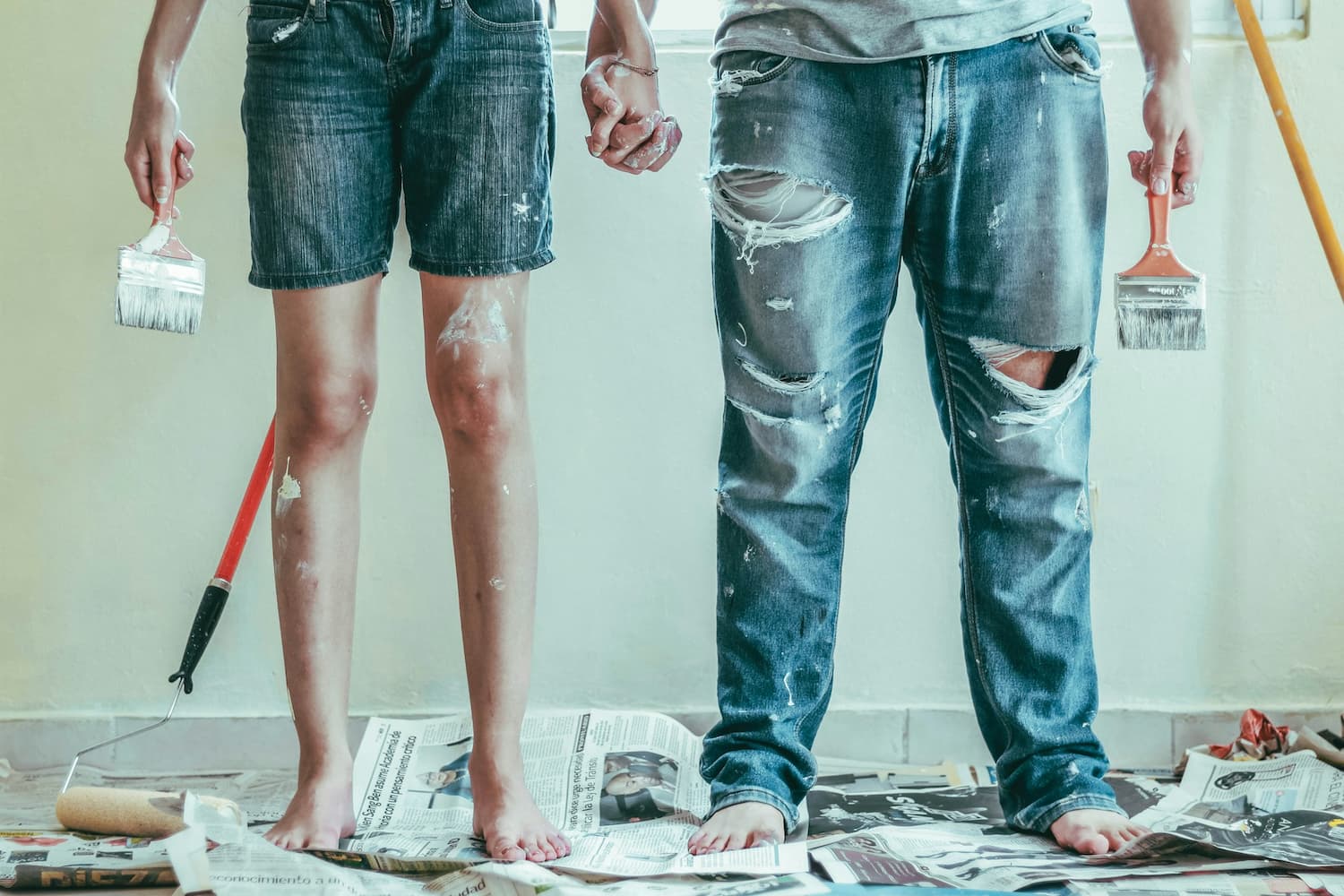 Two investors in paint-splattered jeans holding brushes during a property refurbishment