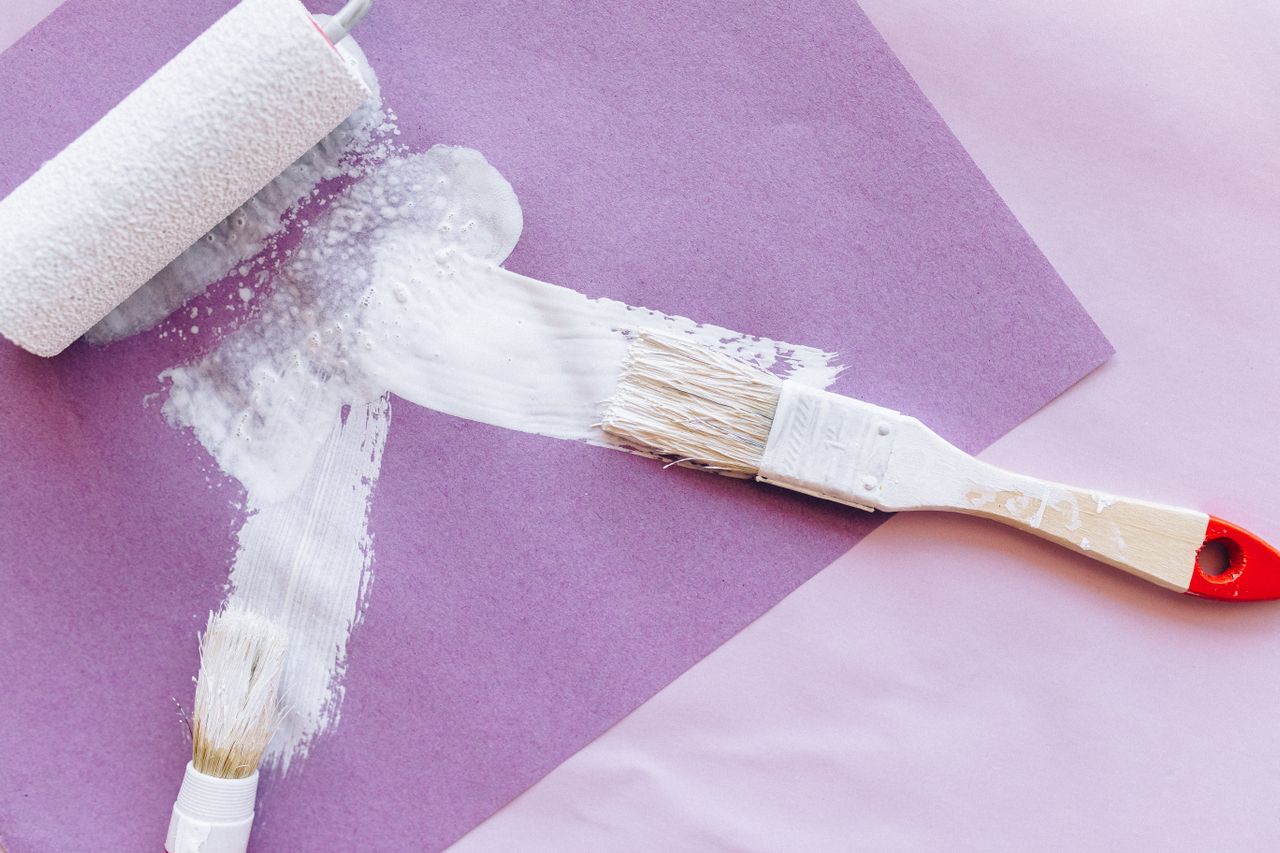 Paint brushes and a roller with white paint, illustrating the refurbish step of the BRRR property strategy