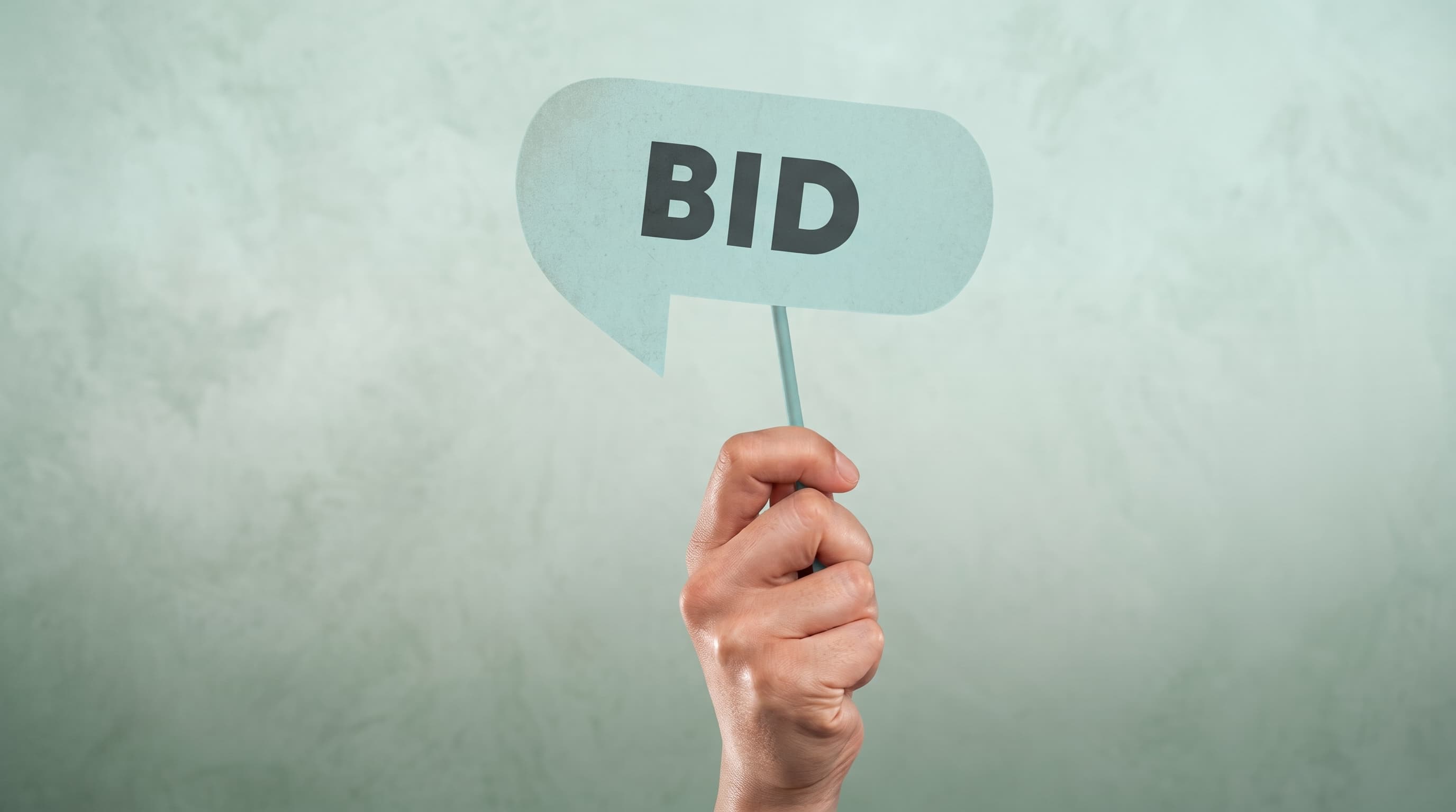 Hand holding a blue BID sign against a pale green wall, representing bidding at a UK property auction