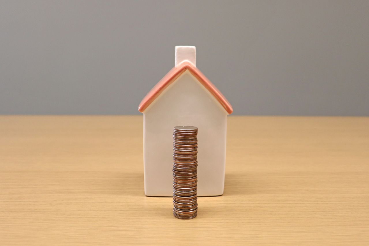 Stack of coins in front of a model house, hiding part of it, representing the cash needed to buy a property below market value