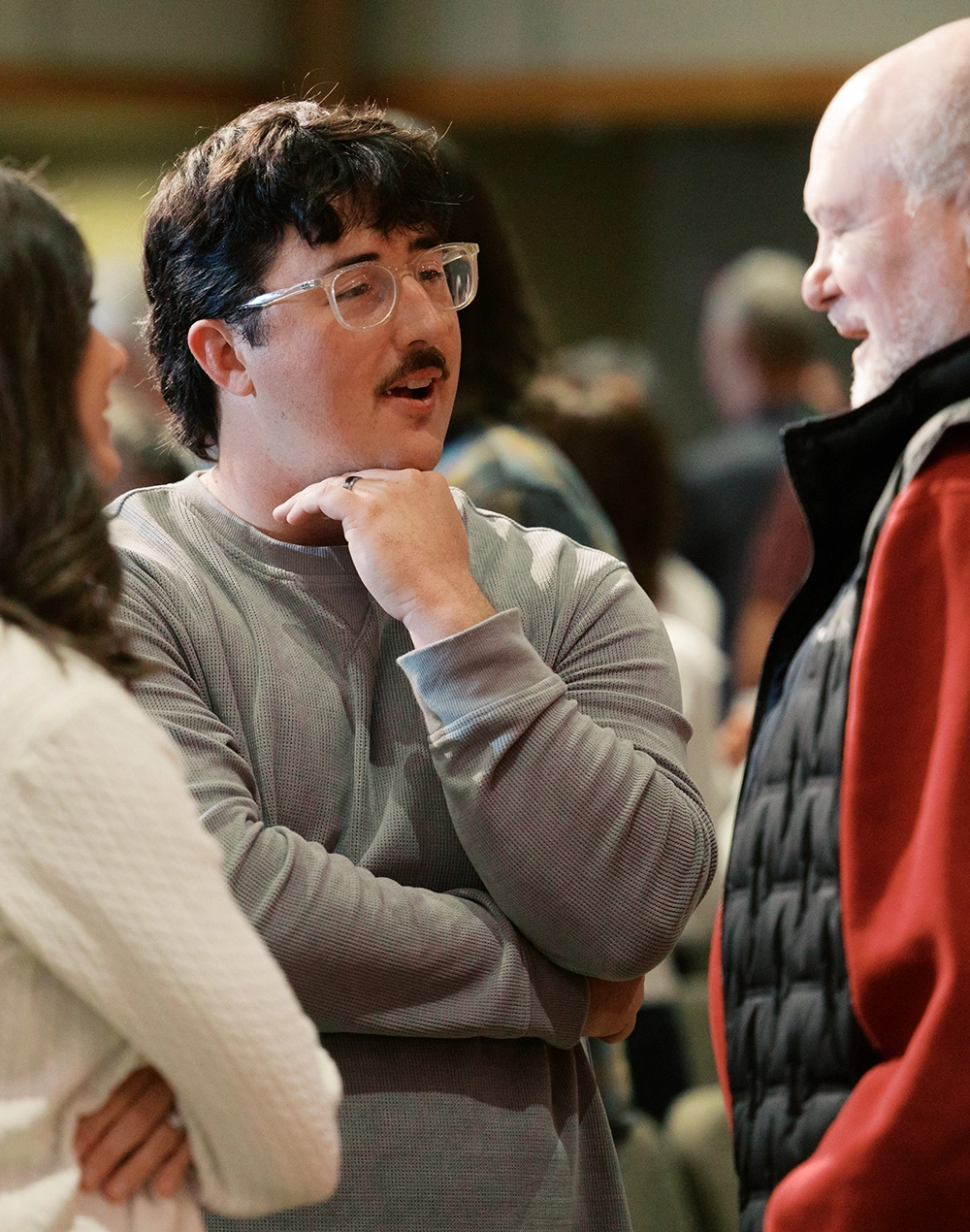 a young man with glasses and a mustache talks to an older man