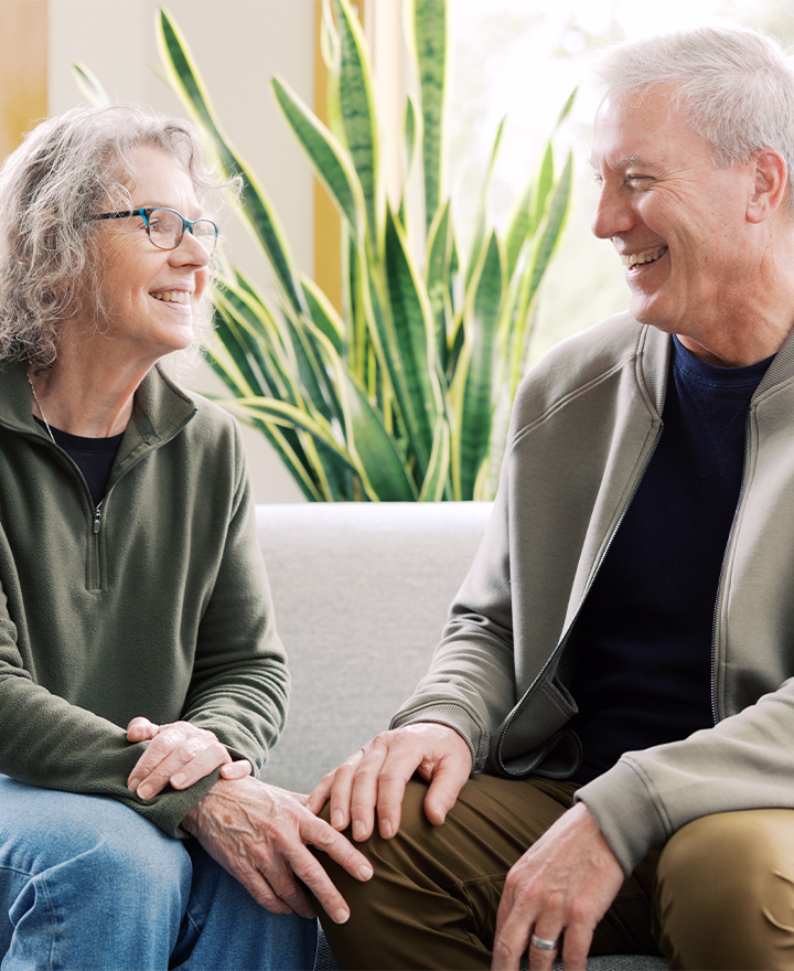 A man and a woman sitting on a couch smiling.