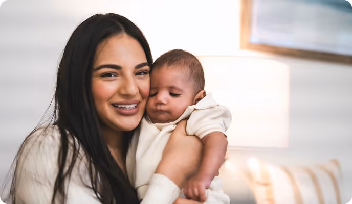 A young woman holds an infant and smiles. 