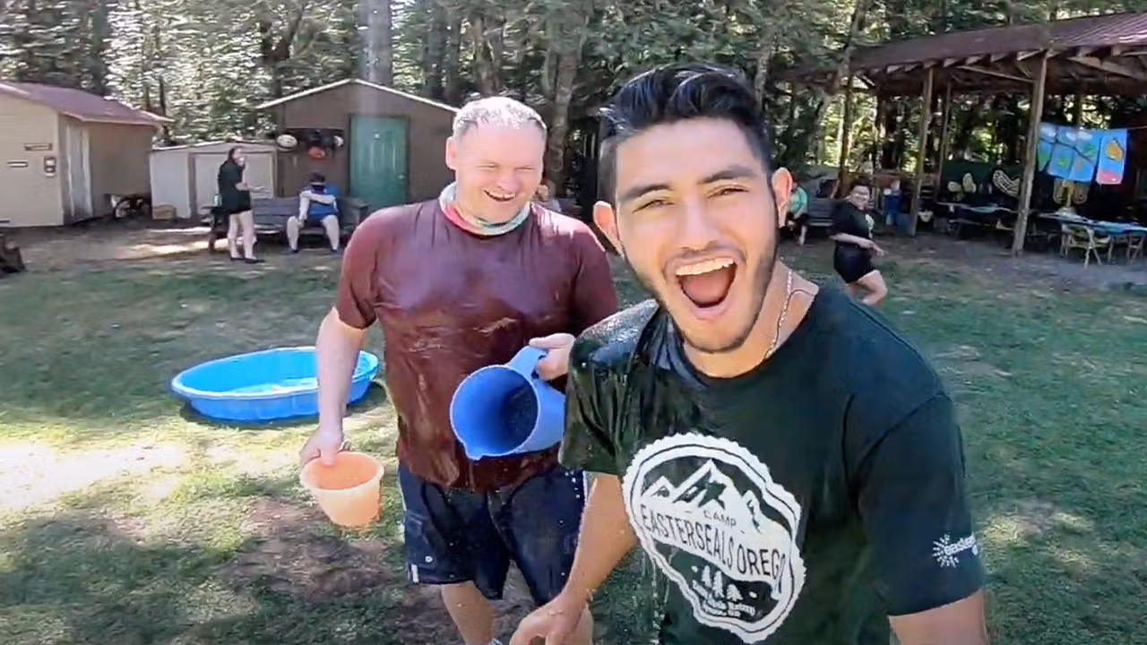 two camp volunteers toss water at each other