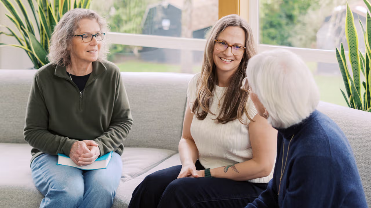 a group of women smile on a couch and talk