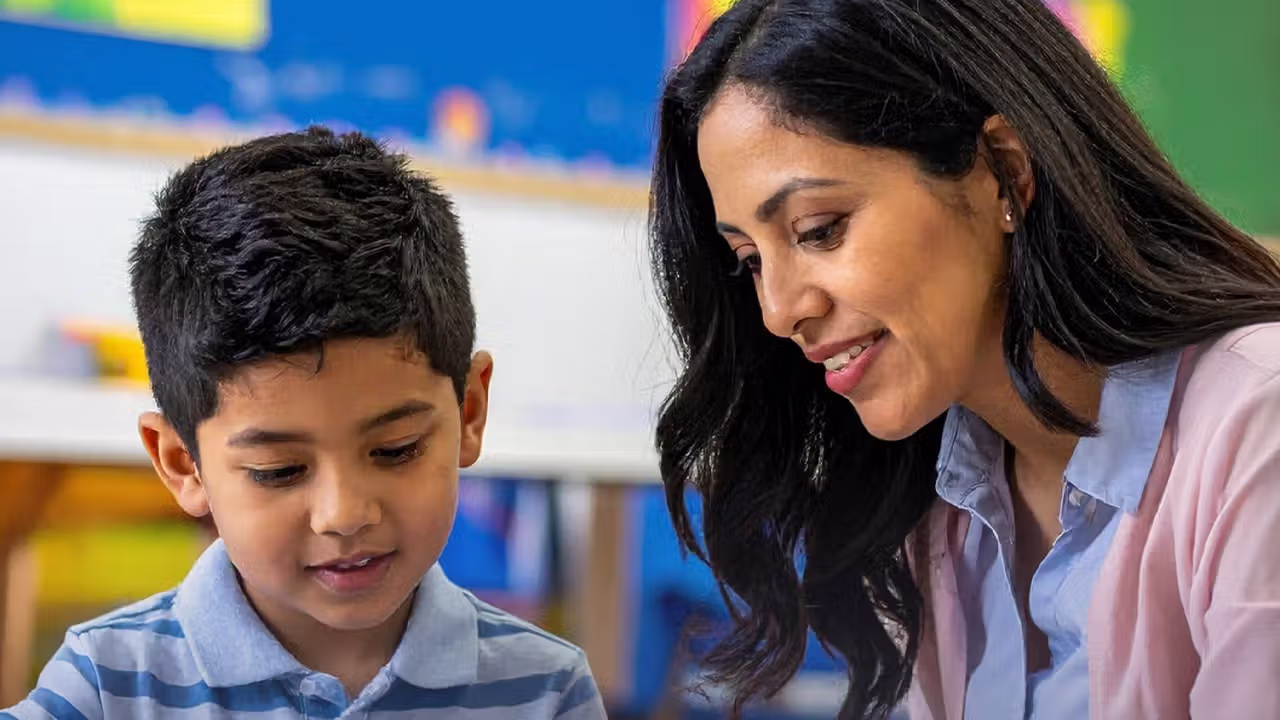 A smiling young boy and mom sit in a classroom together