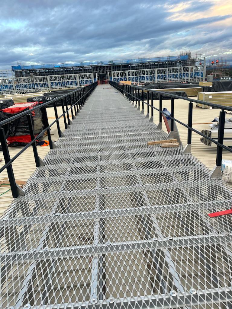 Elevated steel-grating rooftop walkway with handrails.