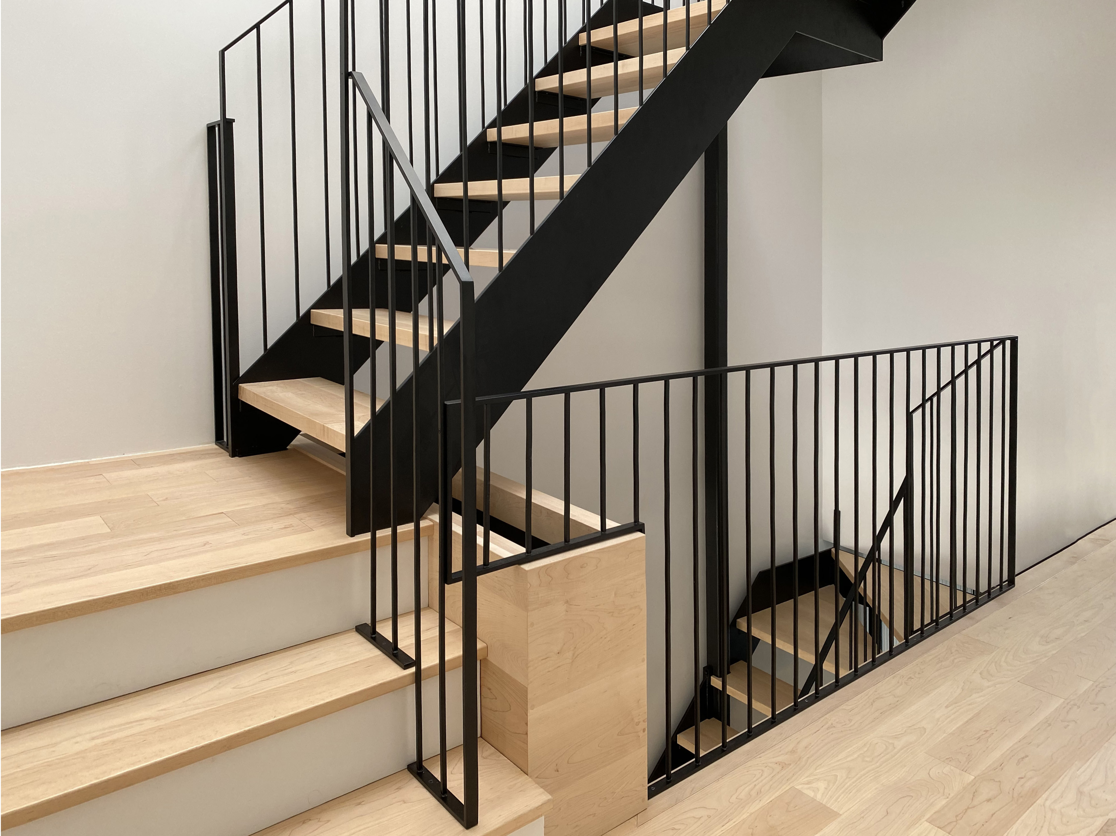 Modern staircase with light wooden steps and black metal railings inside a minimalist interior.