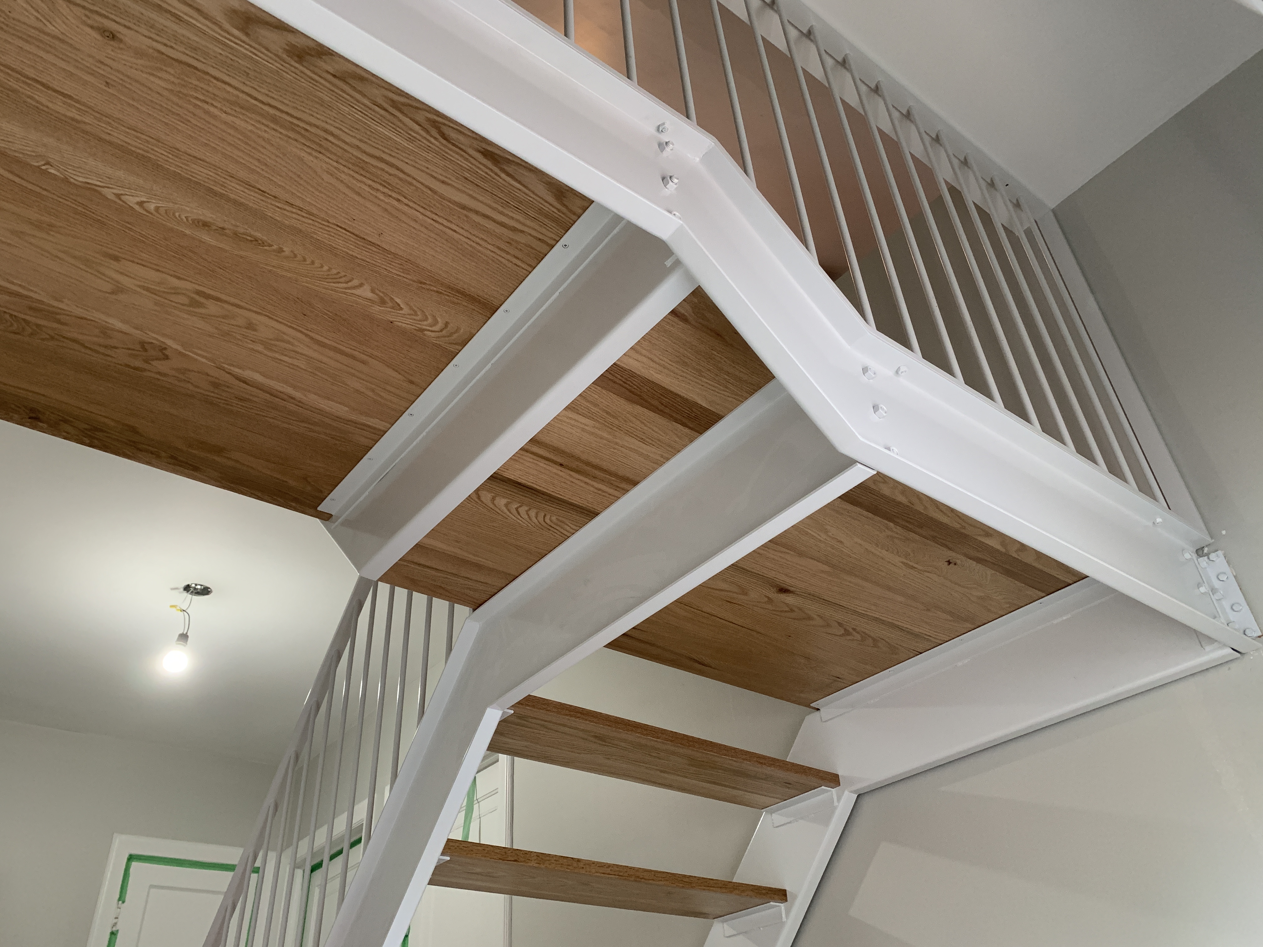 Modern indoor staircase with white metal frame and wooden steps and landing, viewed from below.