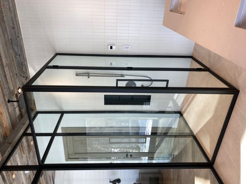 Modern bathroom shower enclosure with black metal frame and glass panels, featuring a rainfall showerhead and tiled walls.
