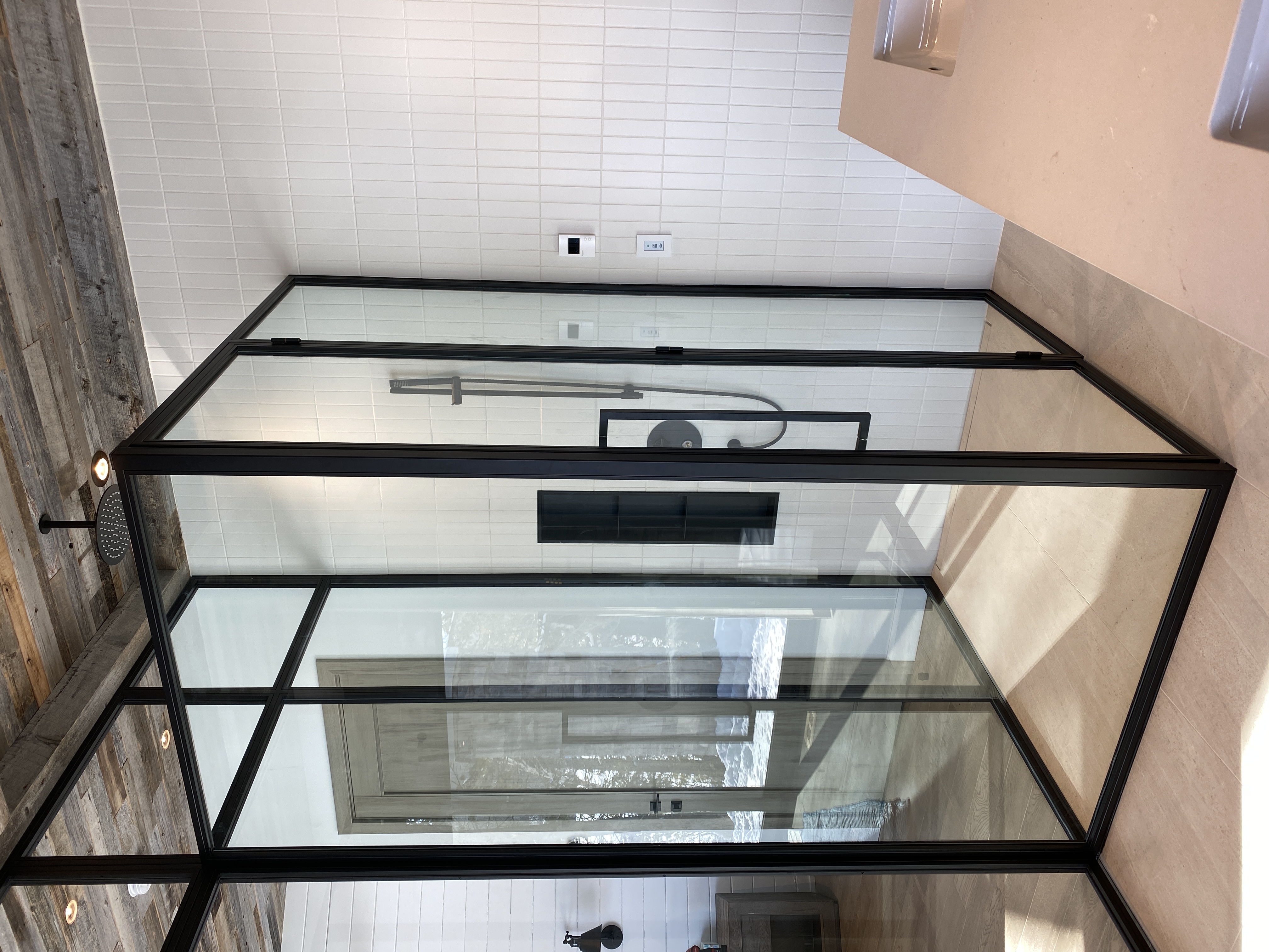 Modern bathroom shower enclosure with black metal frame and glass panels, featuring a rainfall showerhead and tiled walls.