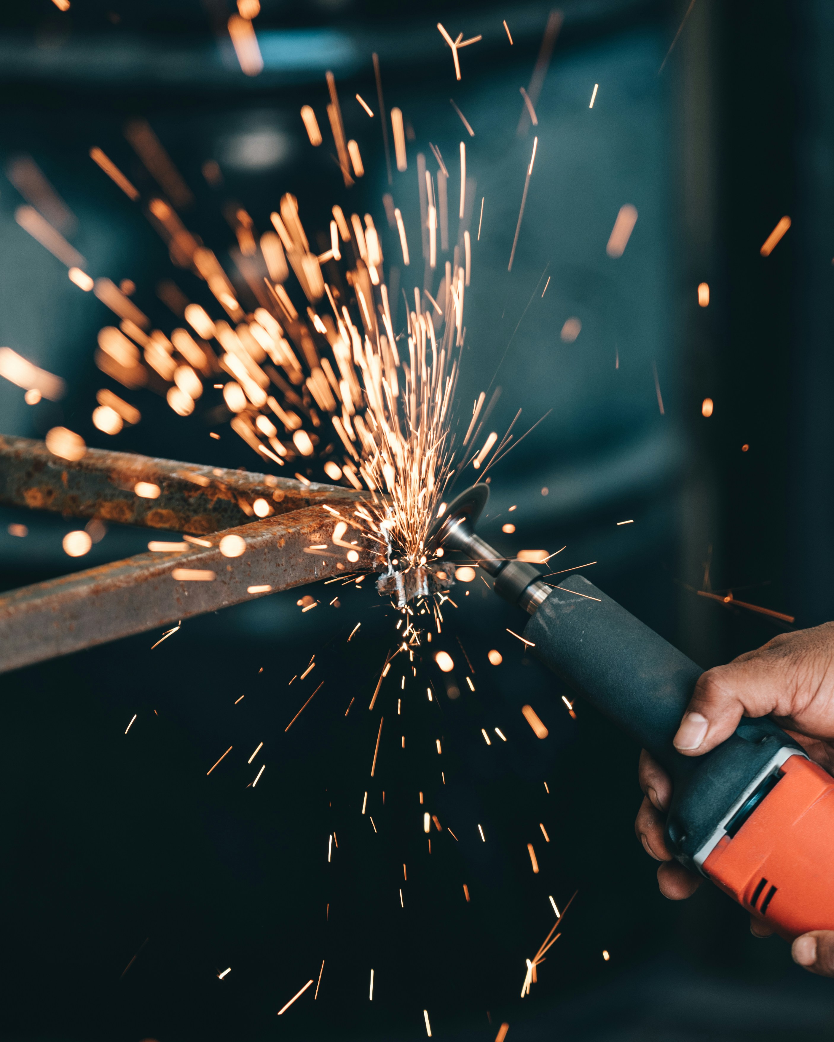 Close-up of a hand using an angle grinder to cut rusted metal, sending sparks flying.