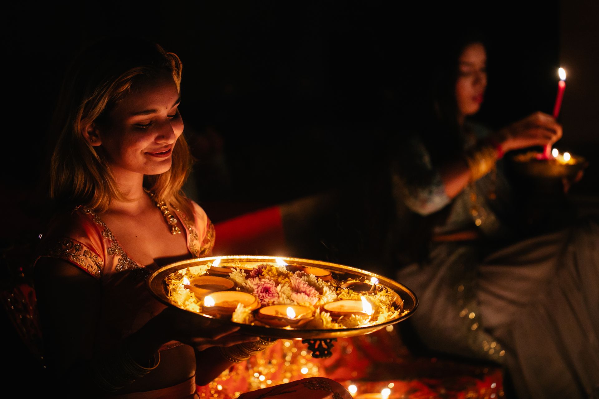 Woman holding a diya-lit puja thali during the Karwa Chauth evening puja