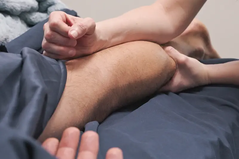 Person receiving a sports massage on their leg with hands applying pressure.