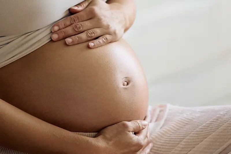 Close-up of pregnant woman gently holding her bare belly with both hands.