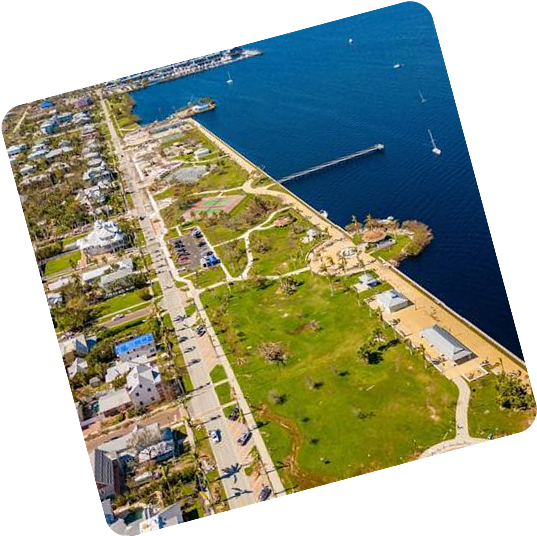 Aerial view of coastal town with green park and pier jutting into blue water