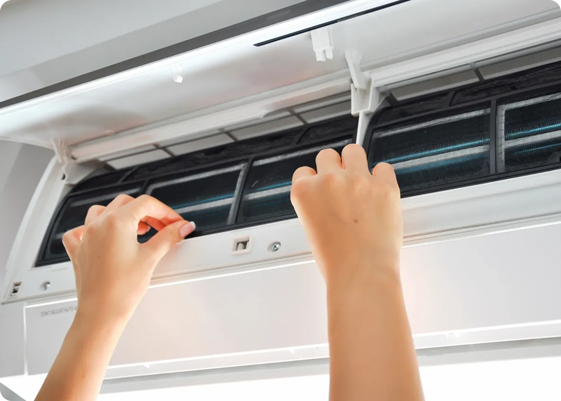 Hands opening and cleaning an air conditioning unit's filter panel