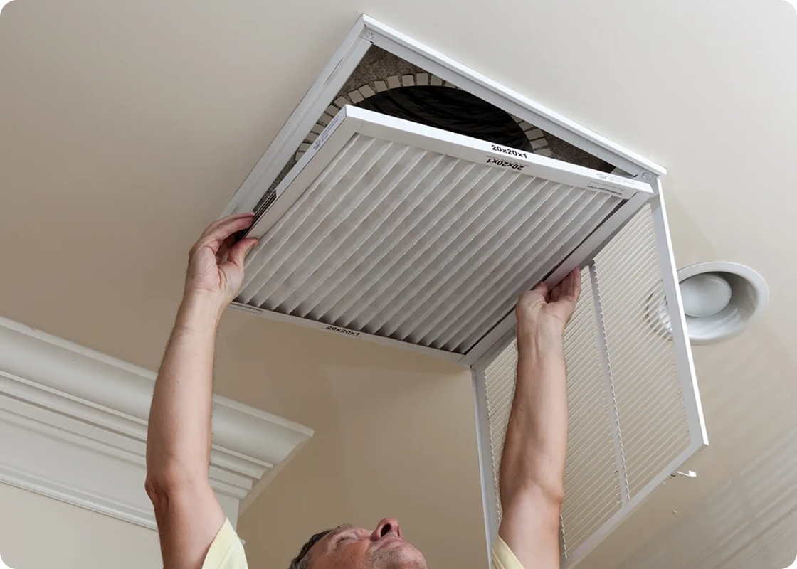 Person removing air filter from ceiling vent in home