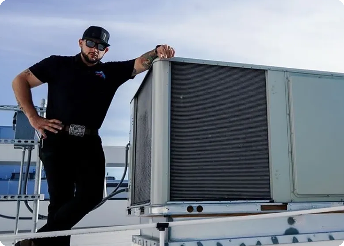 HVAC technician in black standing next to industrial air conditioning unit