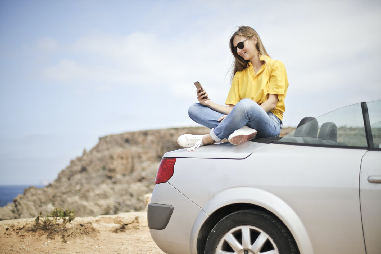 Woman sitting on a car looking at her phone