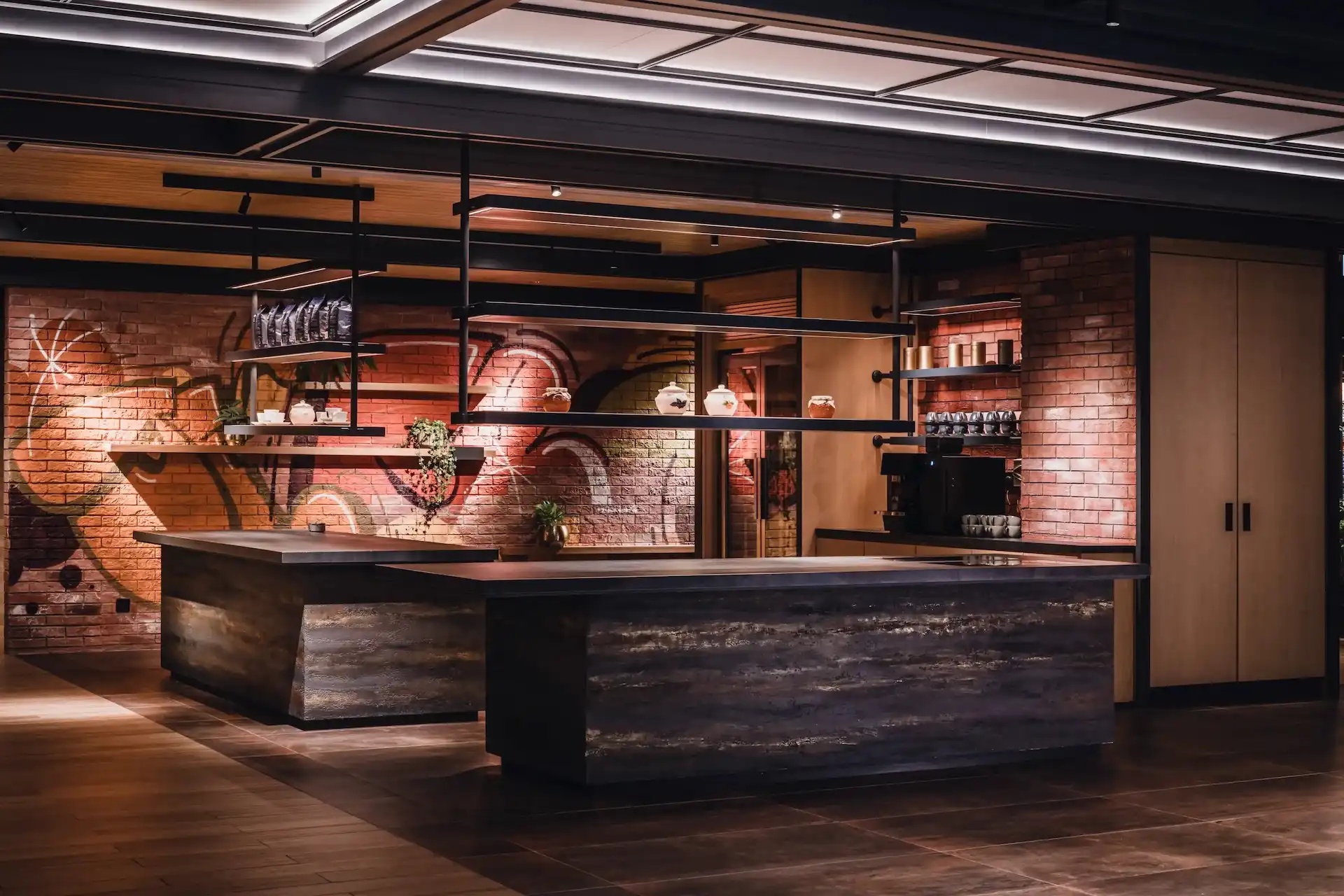 Breakout counter at Hyatt Centric Kuala Lumpur featuring industrial steel shelving, brick feature wall with graffiti mural, dark stone countertop and warm ambient lighting within the lobby space.