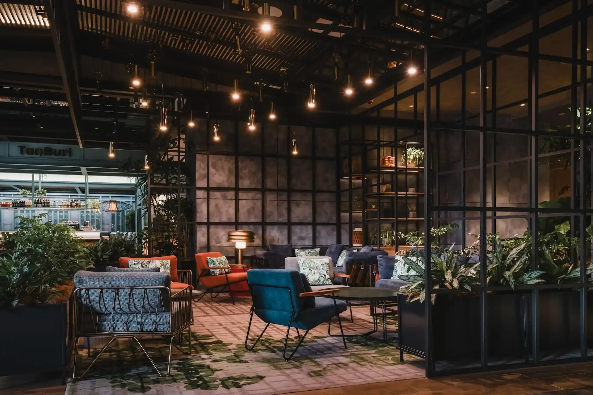 Lobby seating area at Hyatt Centric Kuala Lumpur featuring exposed steel framework, pendant lighting, glass partitions, indoor planting and contemporary lounge chairs with upholstered cushions.