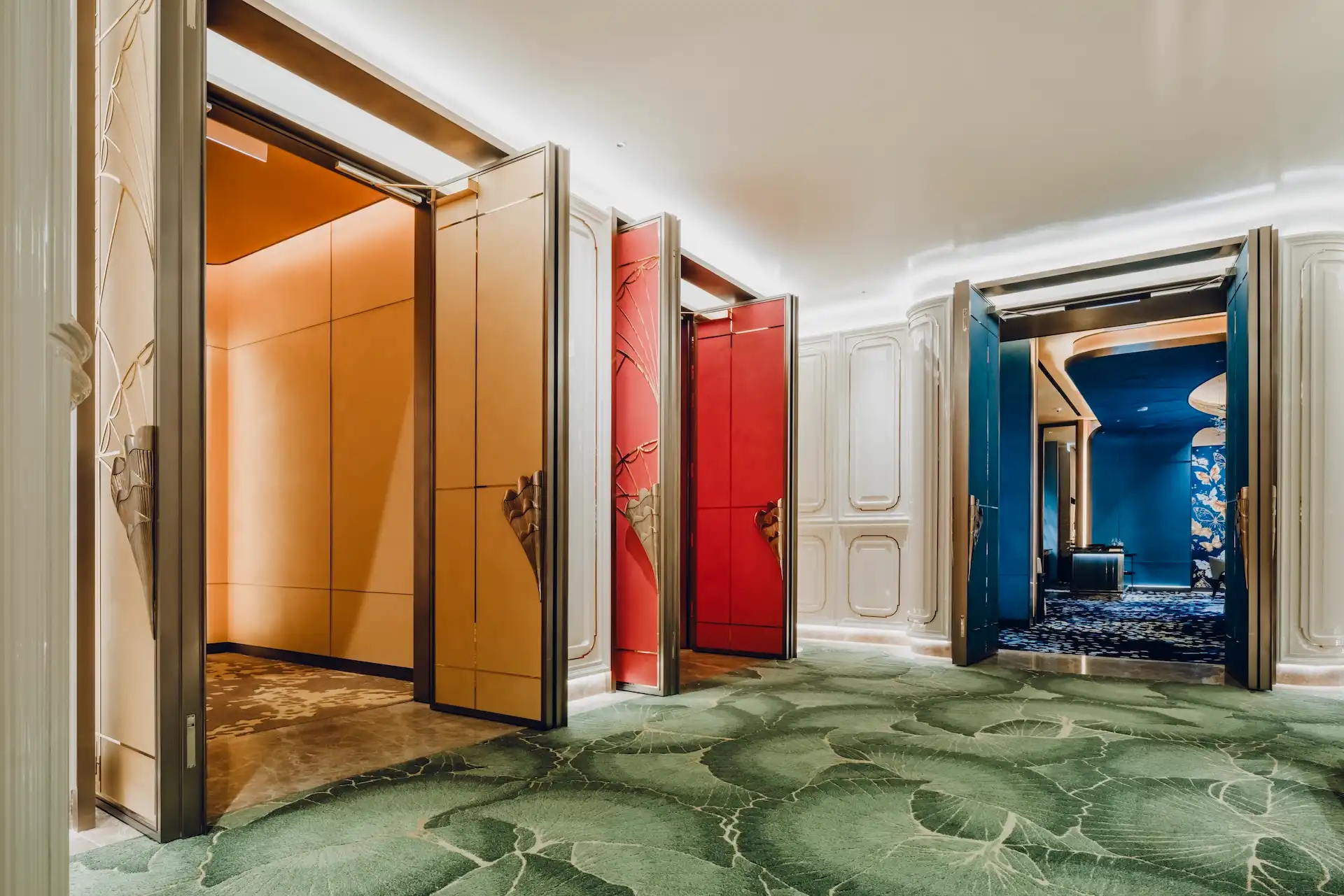 Grand Imperial Court private dining rooms at MGM Macao with open lacquer doors in gold red and blue revealing bespoke interiors sculptural brass handles ivory wall panels and green leaf patterned corridor carpet within a luxury Chinese restaurant design
