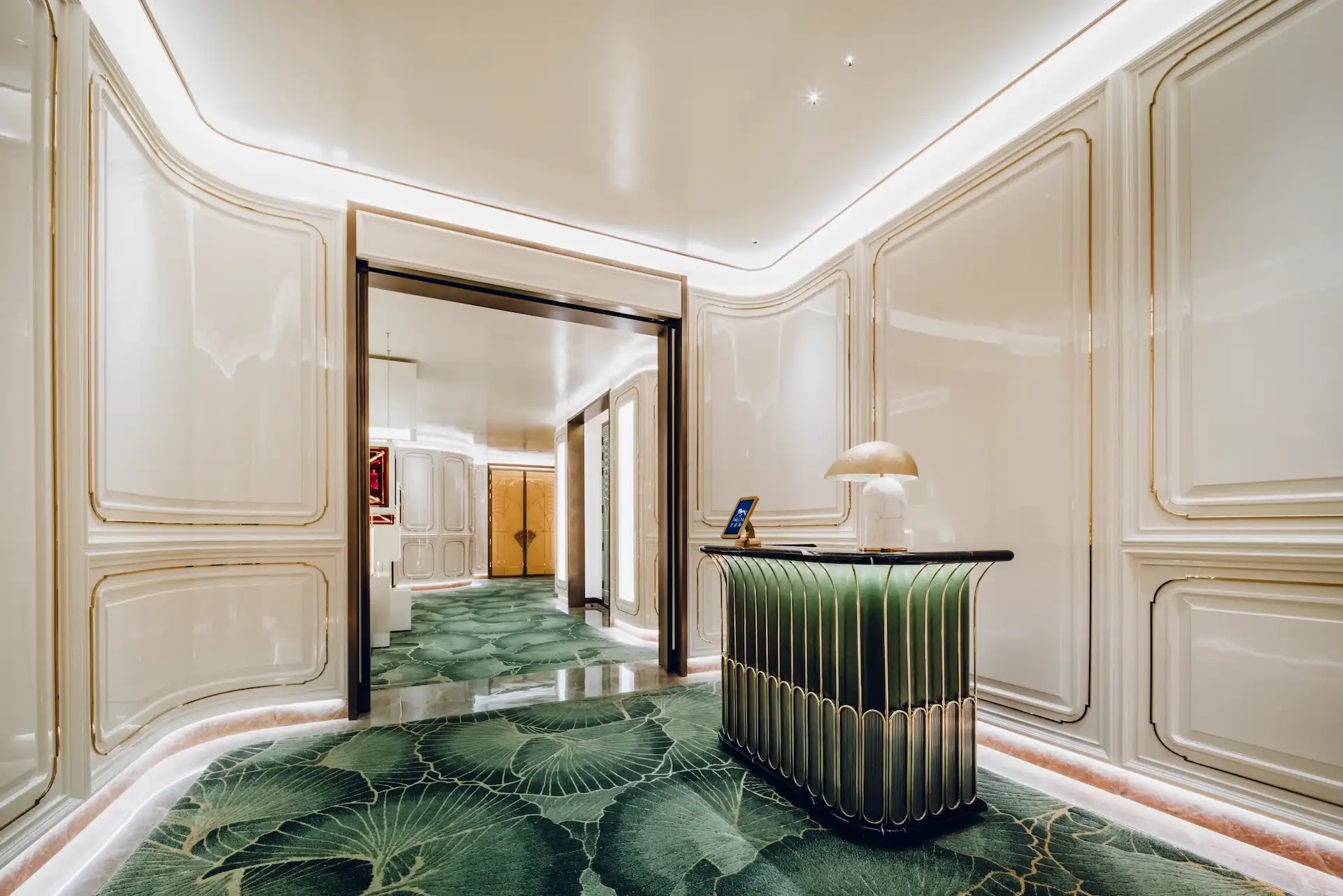 Grand Imperial Court host reception at MGM Macao featuring sculptural green lacquer podium brass detailing ivory wall panels and bespoke leaf patterned carpet within a luxury Chinese restaurant interior