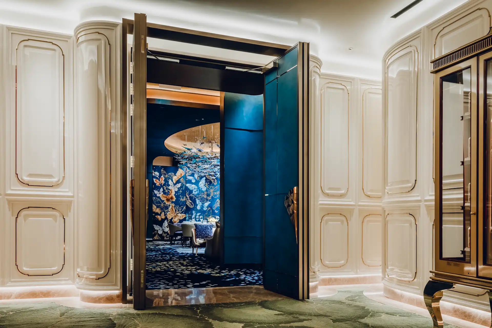 Grand Imperial Court Tapestry Butterfly Wings private dining room at MGM Macao featuring deep blue interior walls butterfly artwork bespoke carpet pattern sculptural brass door handle and open lacquer door within a luxury Chinese restaurant design