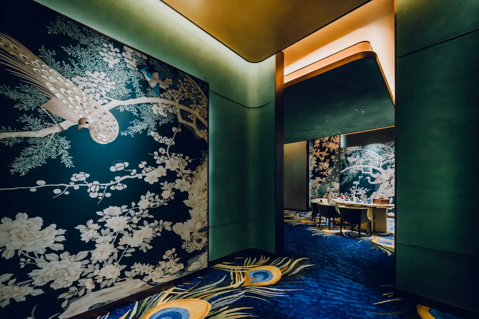 Grand Imperial Court Tapestry Of Feathers private dining entrance at MGM Macao featuring large scale bird and floral wall mural deep green curved wall panels illuminated ceiling detail and bespoke peacock feather patterned carpet leading into the luxury Chinese restaurant dining room