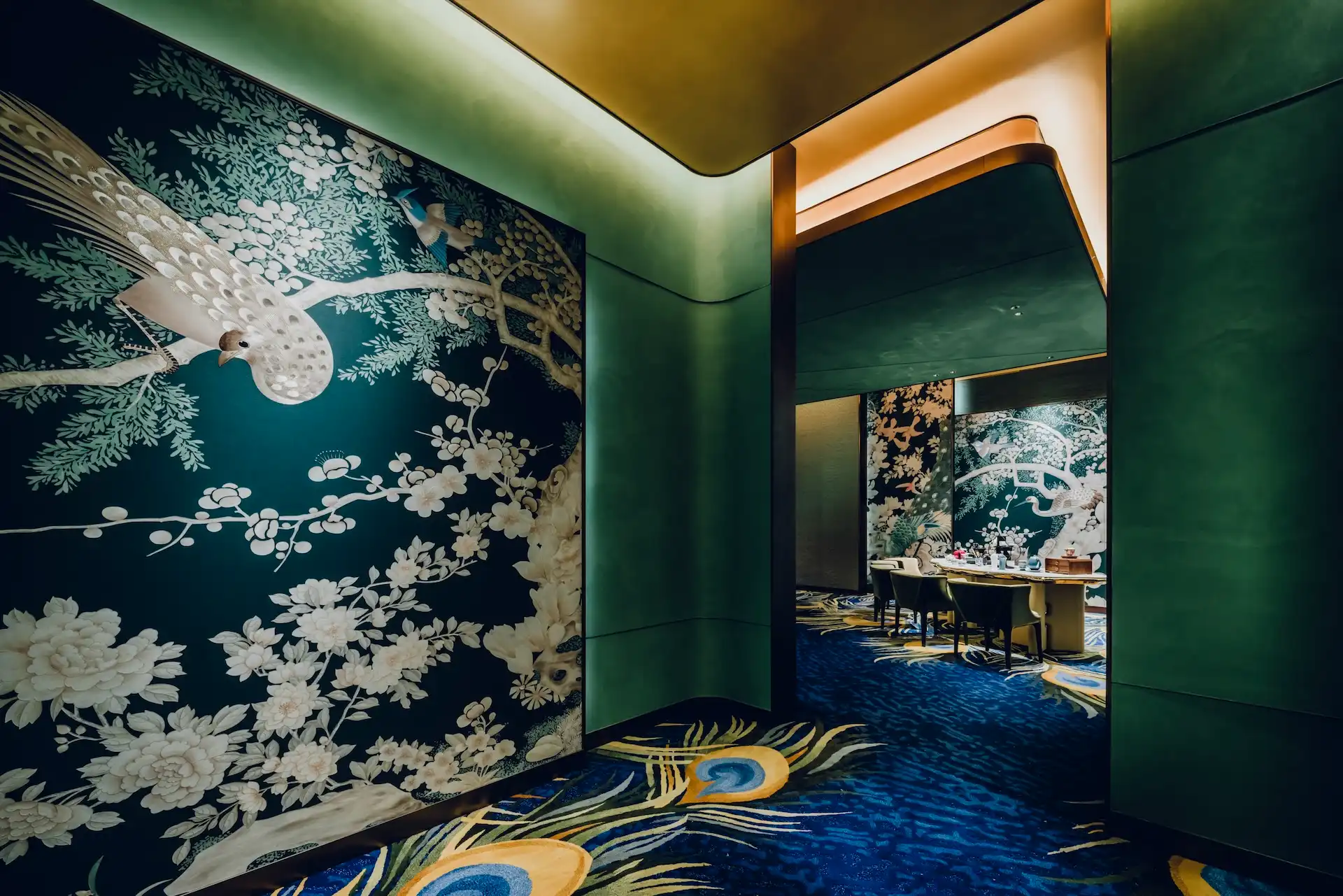 Grand Imperial Court Tapestry Of Feathers private dining entrance at MGM Macao featuring large scale bird and floral wall mural deep green curved wall panels illuminated ceiling detail and bespoke peacock feather patterned carpet leading into the luxury Chinese restaurant dining room