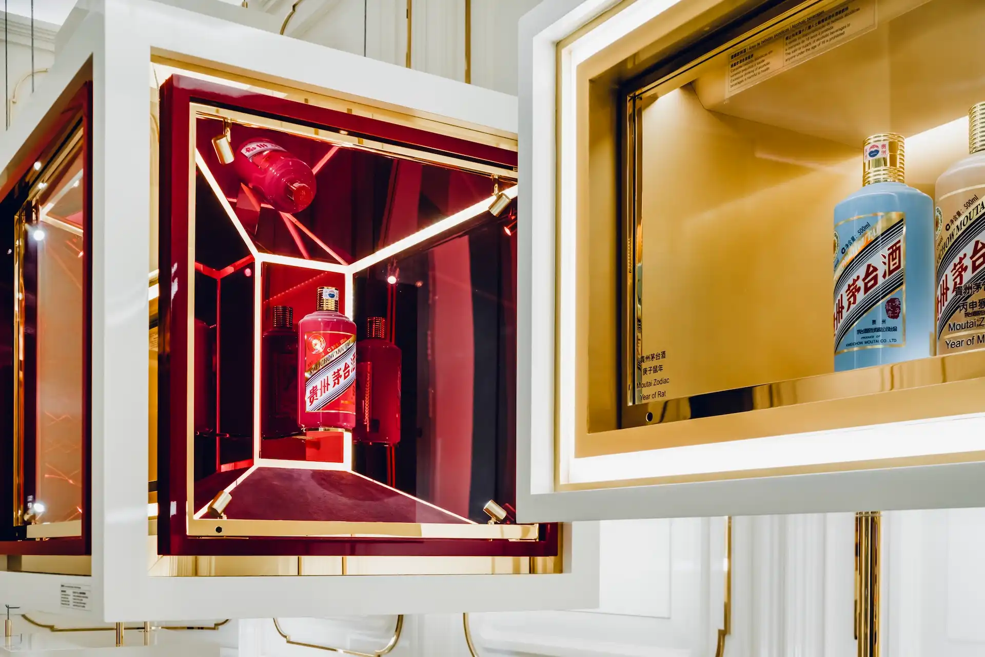 Close up of illuminated Moutai display boxes at Grand Imperial Court MGM Macao featuring mirrored interiors brass frames red lacquer detailing and suspended bottle presentation within a luxury Chinese restaurant interior